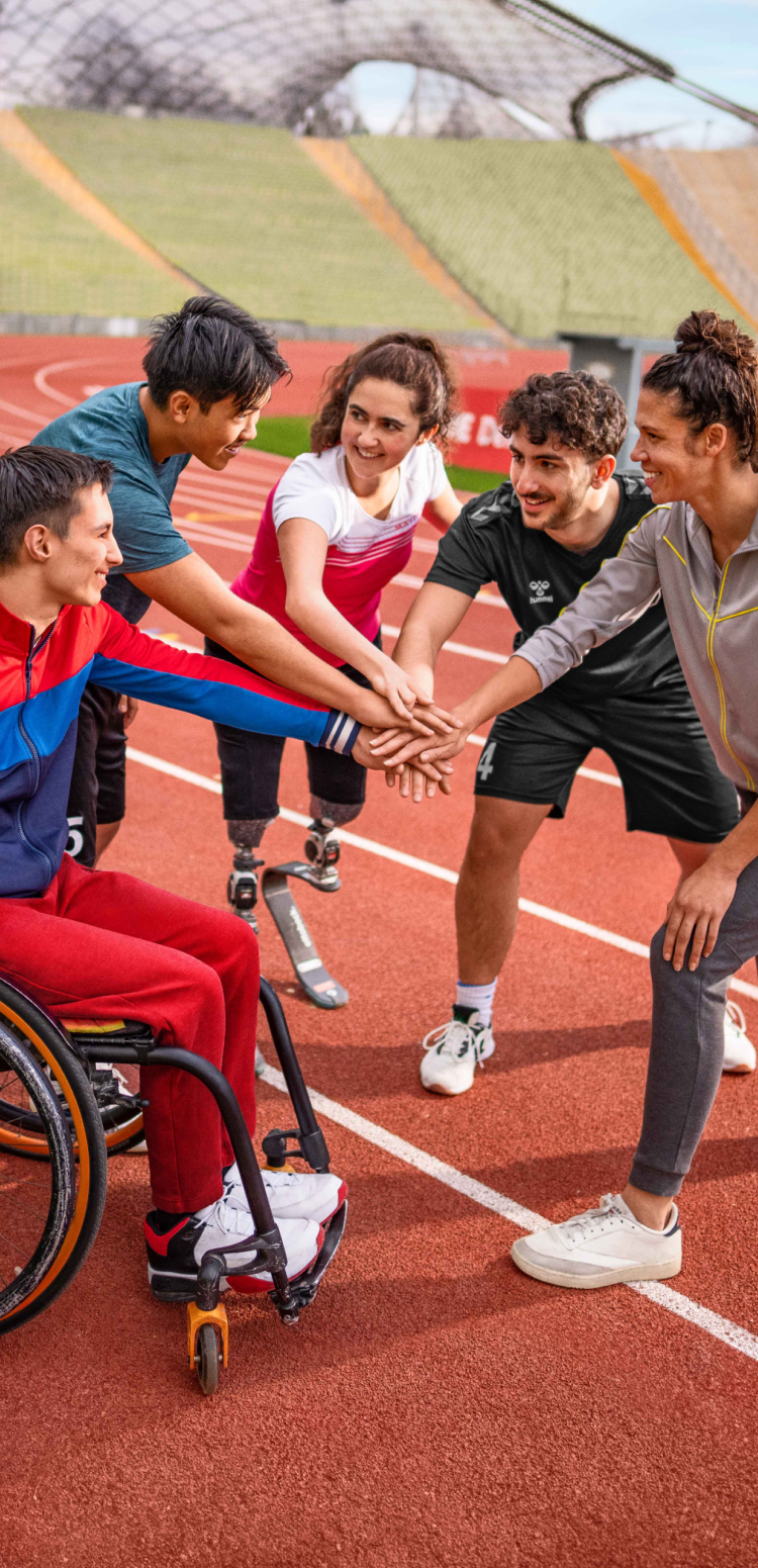 Menschen mit und ohne Behinderung legen ihre Hände aufeinander, um sich auf einer Tartanbahn auf ein sportliches Event einzustimmen.