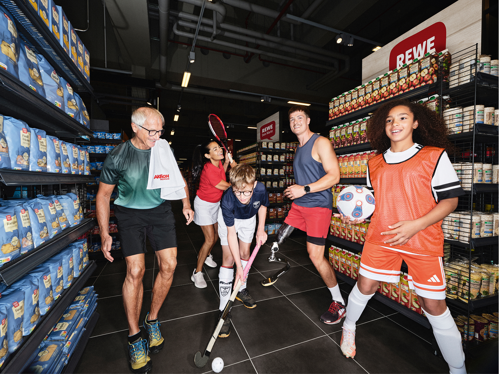 Diverse Sportler:innen haben gemeinsam Spaß in einem REWE Markt und zeigen, was ihre Sportarten besonders macht