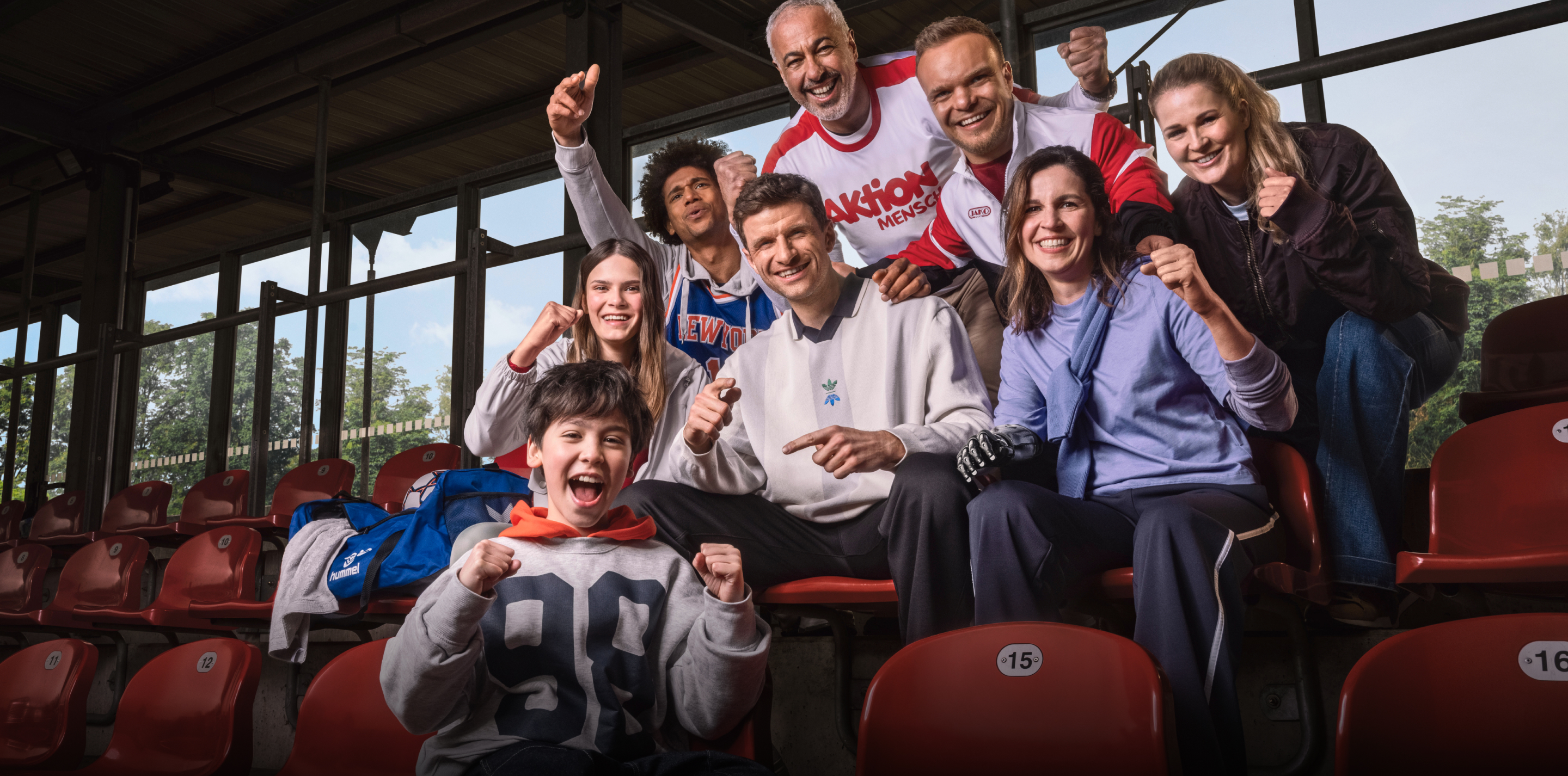 Sportler und Fans jubeln mit Thomas Müller und Niko Kappel auf einer Sportplatz-Tribüne