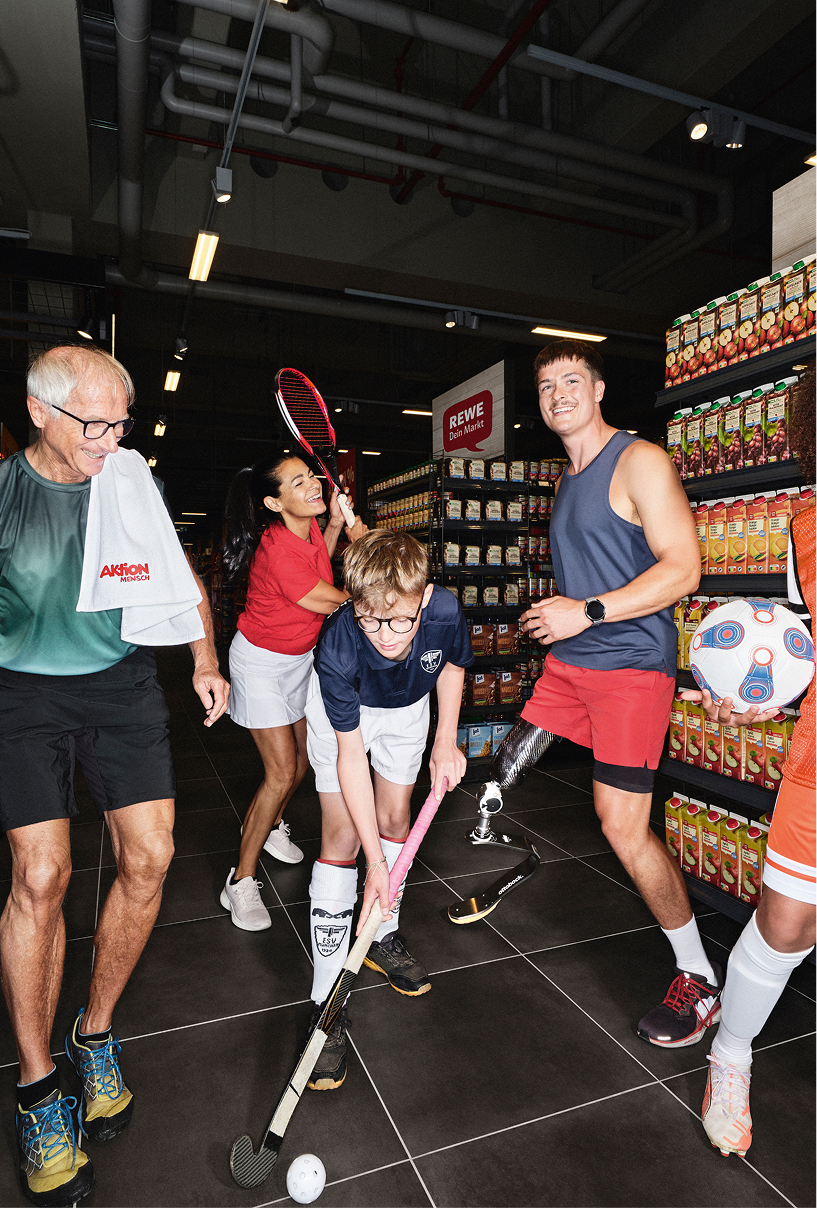 Diverse Sportler:innen haben gemeinsam Spaß in einem REWE Markt und zeigen, was ihre Sportarten besonders macht