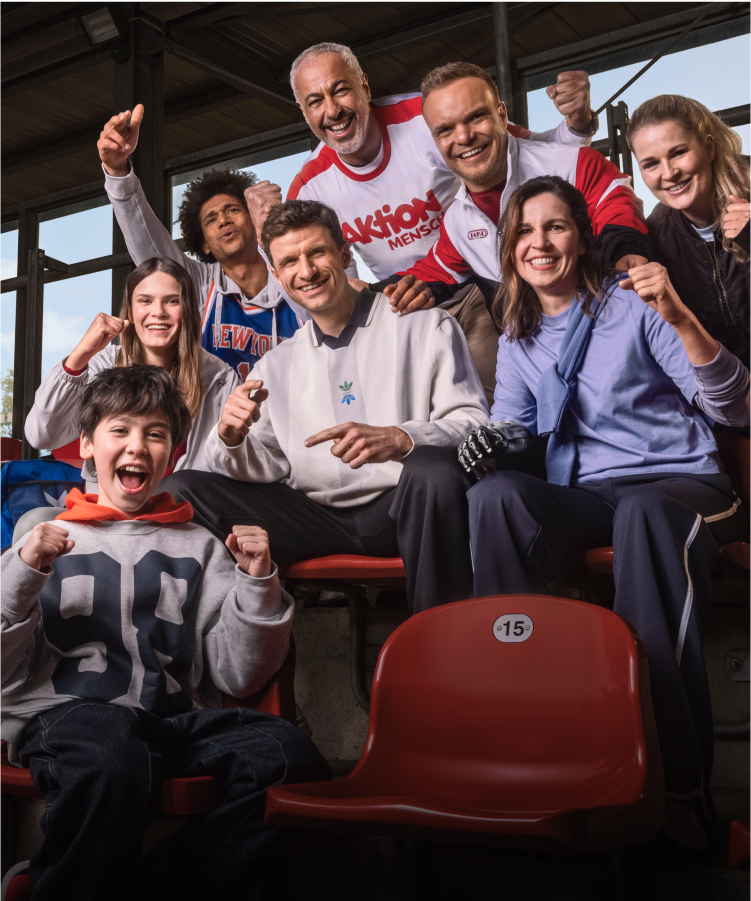 Sportler und Fans jubeln mit Thomas Müller und Niko Kappel auf einer Sportplatz-Tribüne
