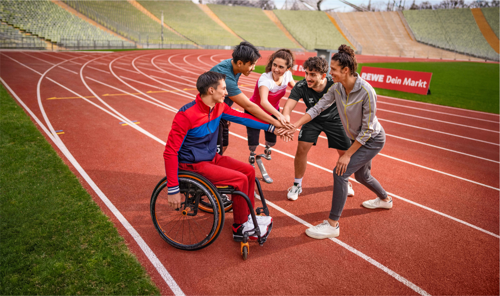 Menschen mit und ohne Behinderung legen ihre Hände aufeinander, um sich auf einer Tartanbahn auf ein sportliches Event einzustimmen.